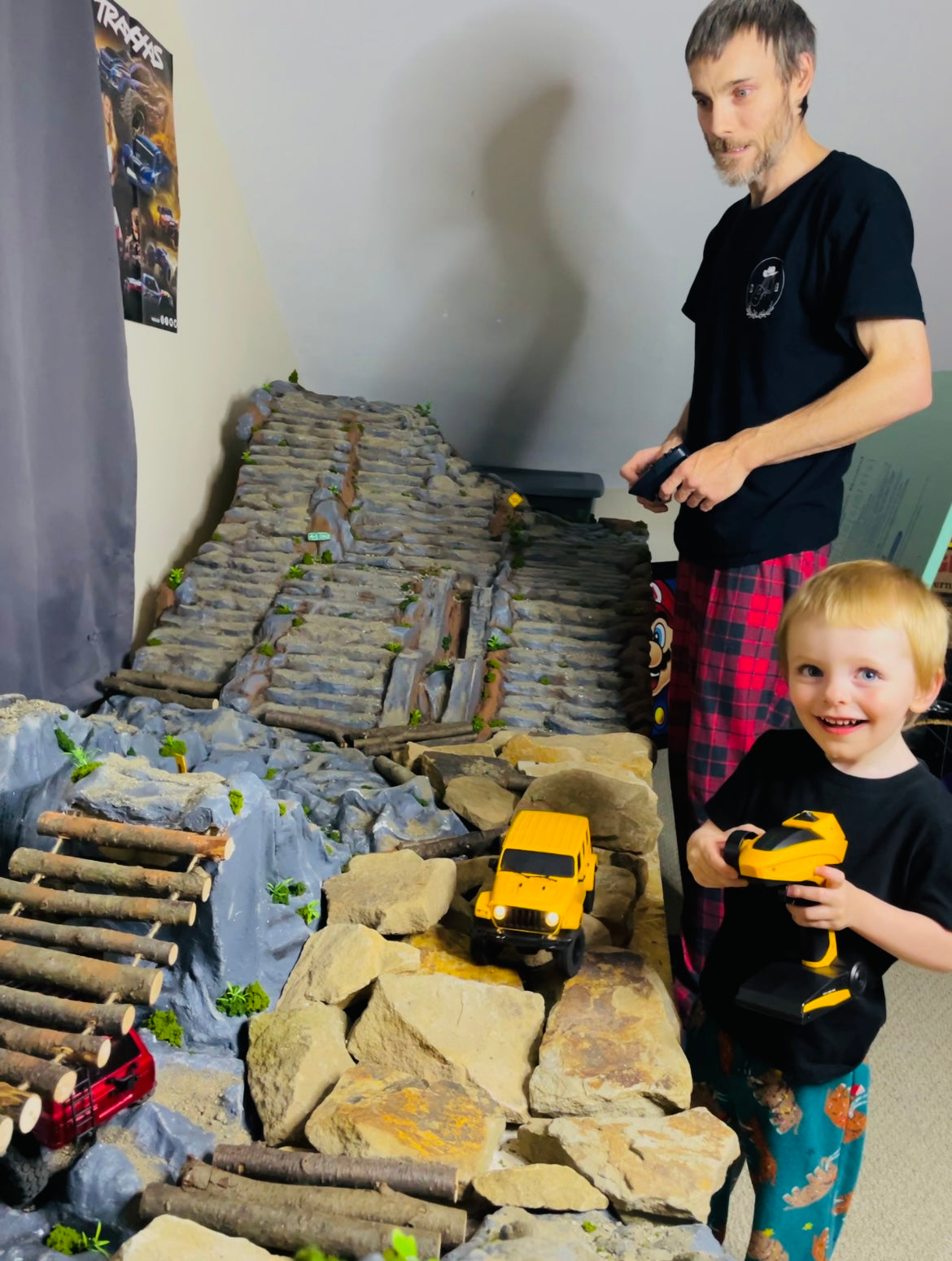 Father and son playing with RC crawler models on an indoor rock climbing obstacle course.