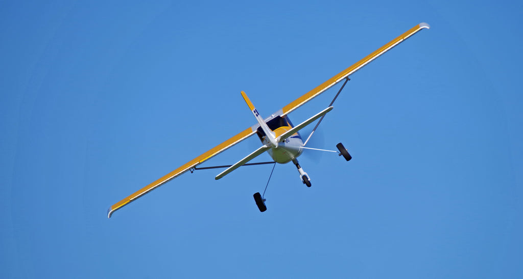 yellow RC trainer plane flying against clear blue sky