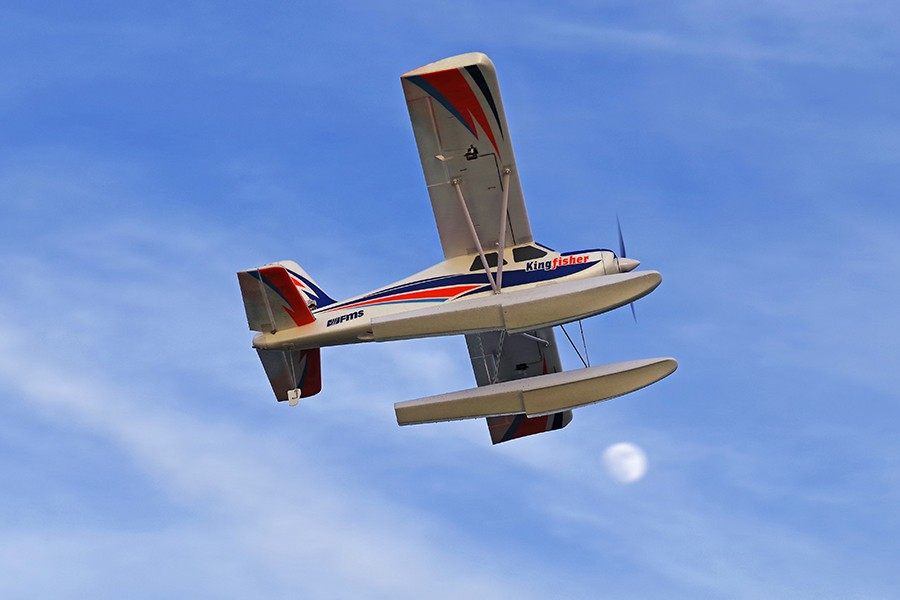 FMS 1400mm Kingfisher PNP seaplane in flight with blue sky and a faint moon.