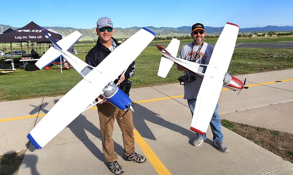Two RC hobbyists holding large RC planes on a runway, featuring a blue and white Cessna aircraft 182 and a red-accented model airplane, perfect for beginner RC flying and adults.