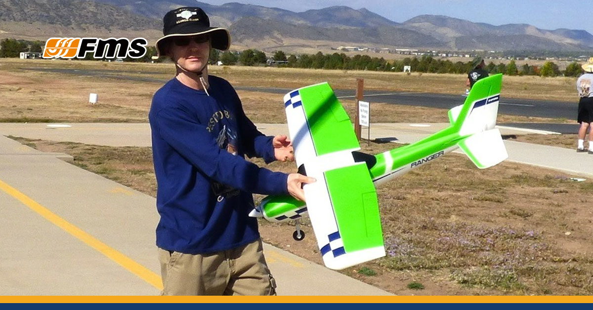 FMS Hobby pilot holding a green and white Ranger RC airplane at an outdoor flying field