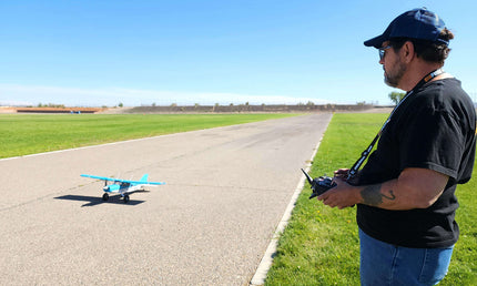 An RC pilot holding a transmitter while controlling a blue and white FMS high-wing RC airplane on a paved runway