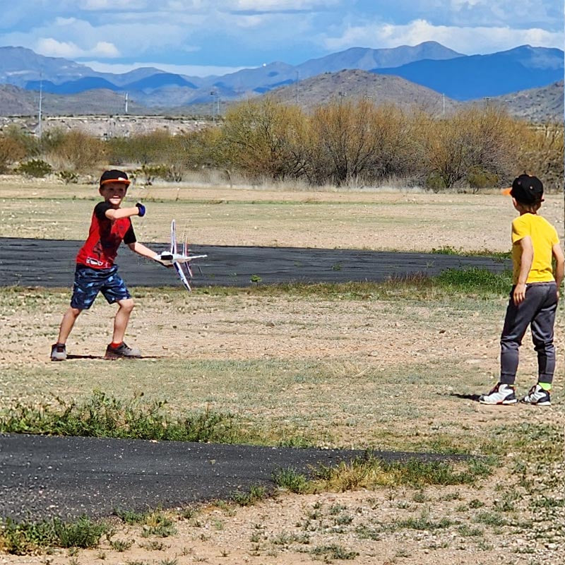 Children playing outdoors, preparing to launch FMS Alpha Hand-Launched Jet in open field.