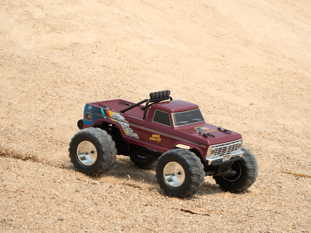 The FMS RC Monster Truck "High Roller" edition sits on a gravel slope, highlighting its chrome rims and roll bar