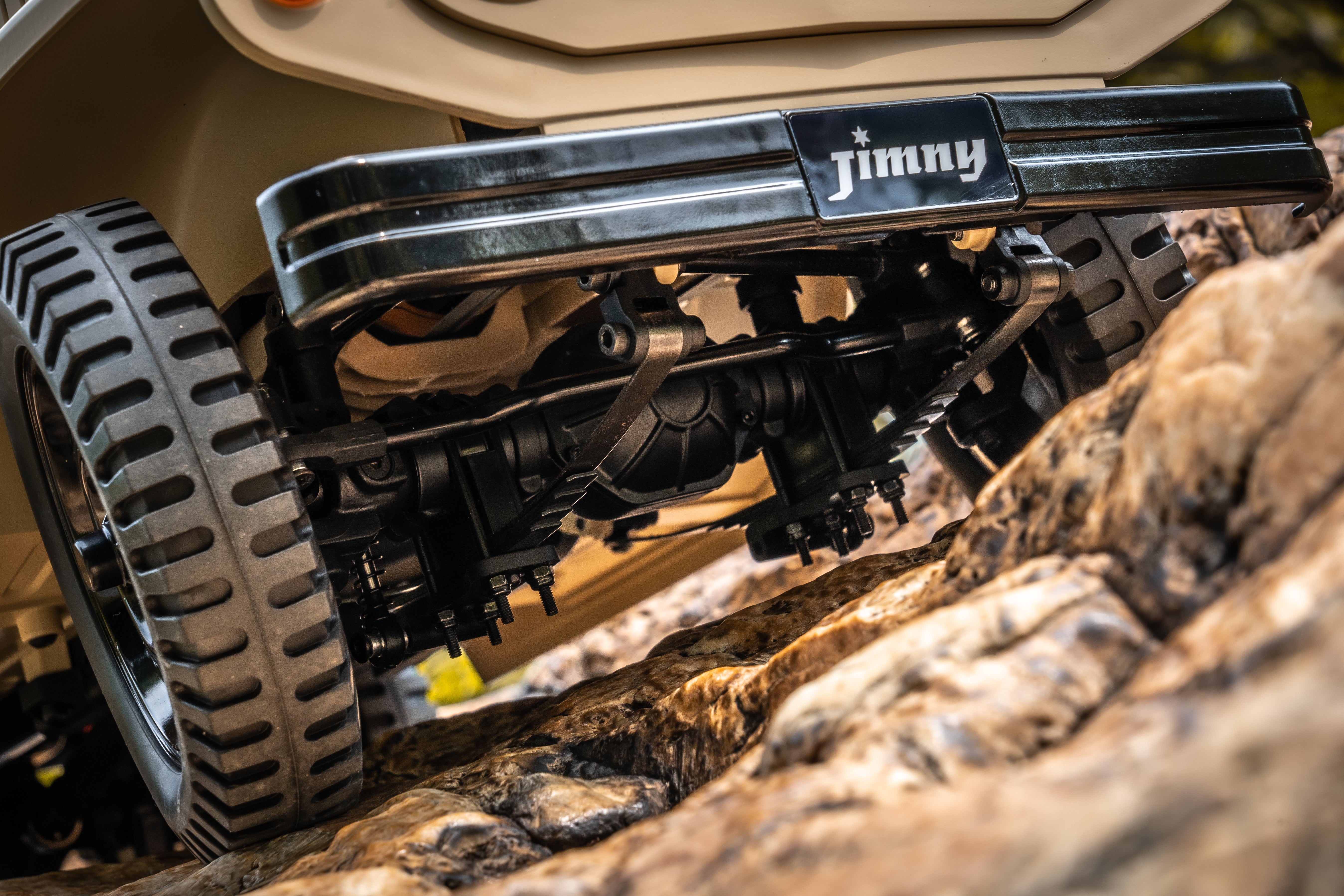 FMS 1:6 Jimny RS Brown model with off-road tires and detailed suspension on rocks.