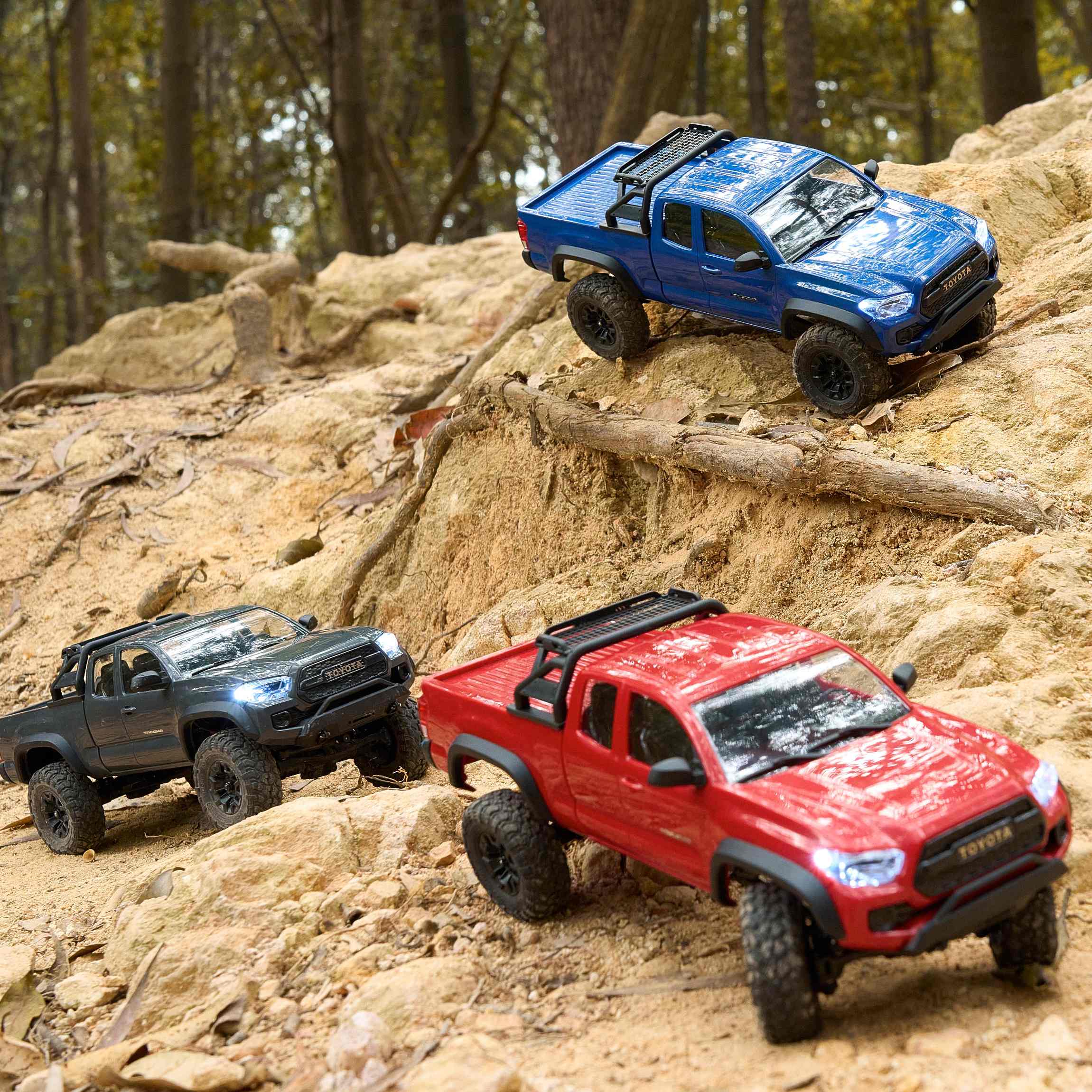 The image depicts three RC Toyota Tacoma trucks navigating a rugged, outdoor terrain, suggesting an exciting off-road adventure.