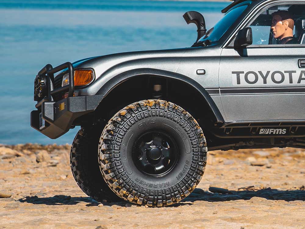 Close-up of an FMS Super Marsher knobby tire on a 1/10-scale RC crawler with sand packed into the tread lugs