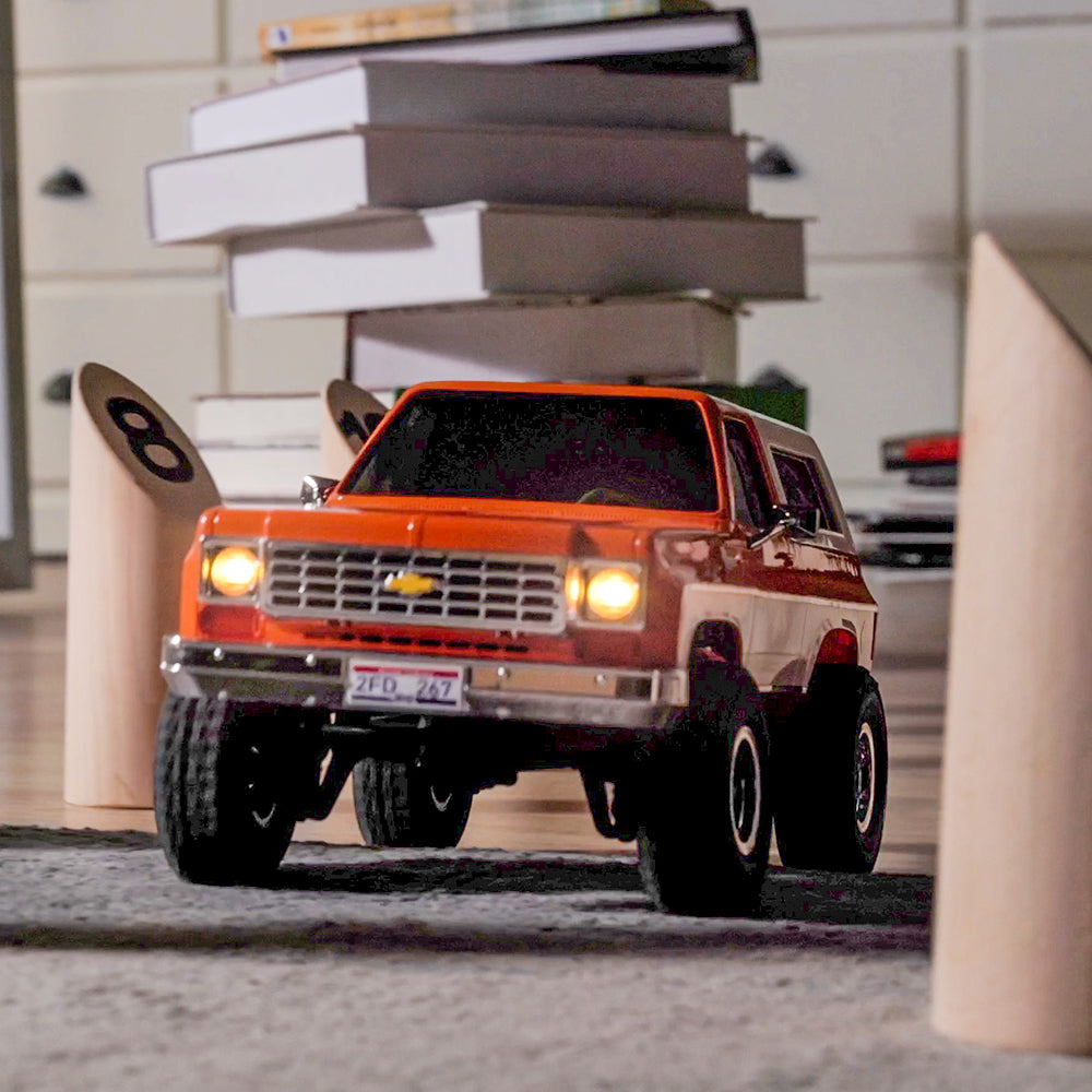 Orange FMS 1:24 FCX24 K5 Blazer RC car with brown/white stripes, chrome grille, lit headlights, and '2FD 267' plate.