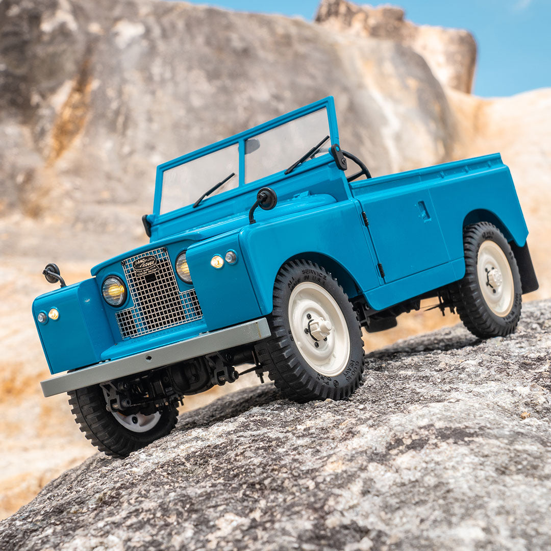 Blue FMS 1:12 Land Rover Series II RTR model off-roading on rocky terrain.