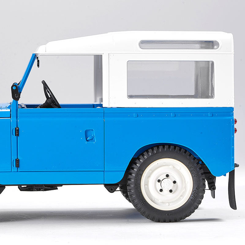 Blue 1:12 FMS Land Rover Series II RTR model with white roof, visible steering wheel and door handle.