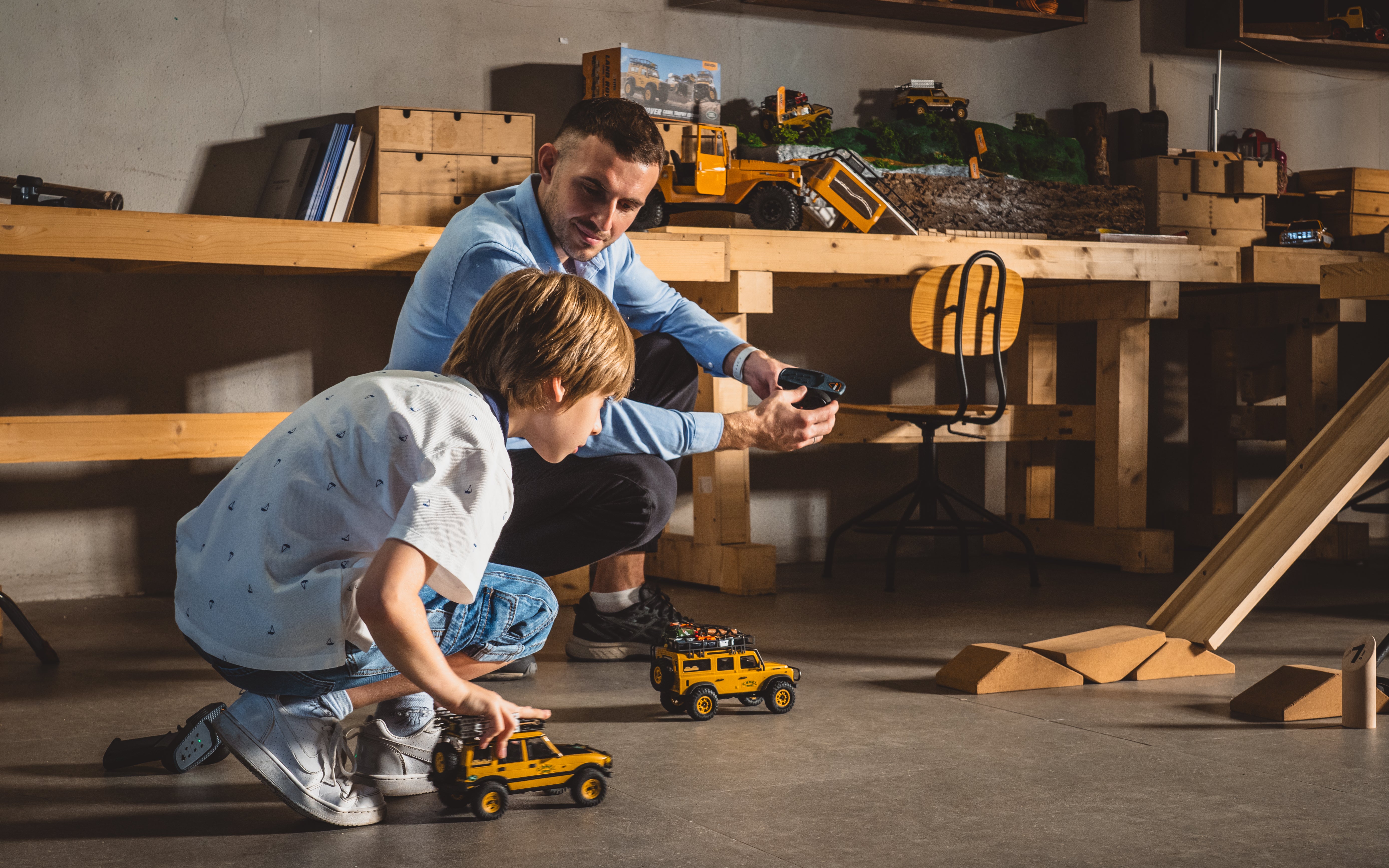 Father and child driving yellow mini RC trucks through an indoor obstacle course