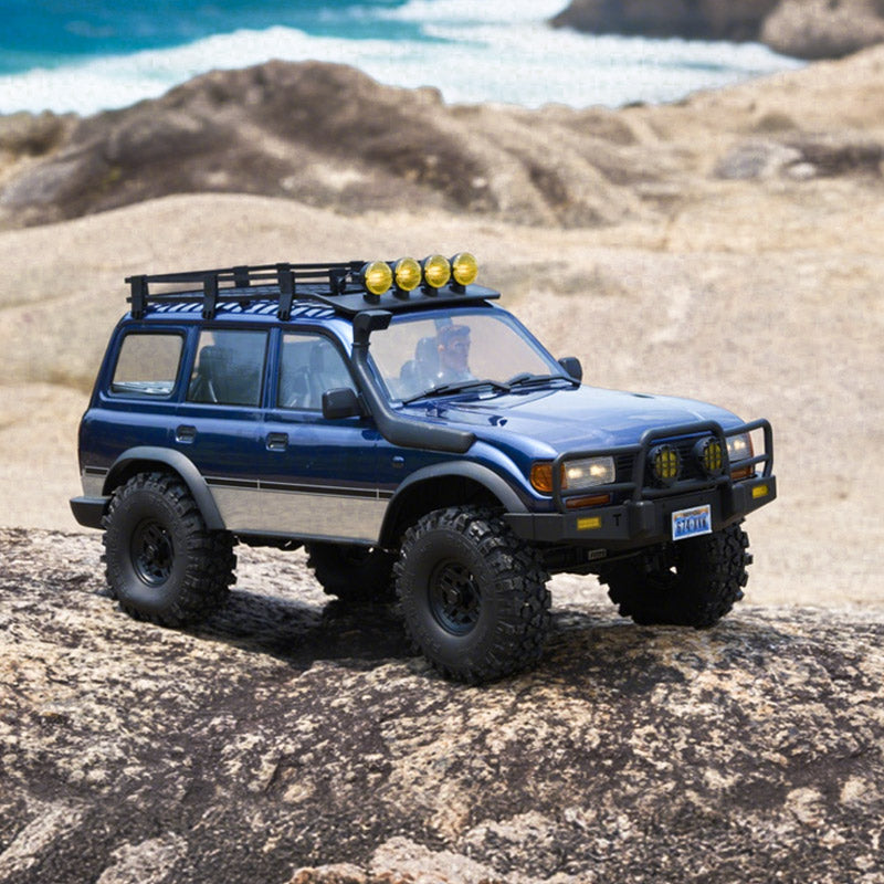 FMS 1:10 FCX10 PRO Brushless Toyota Land Cruiser LC80 RS V2 RC crawler on rocks, blue, with roof rack and spotlights.