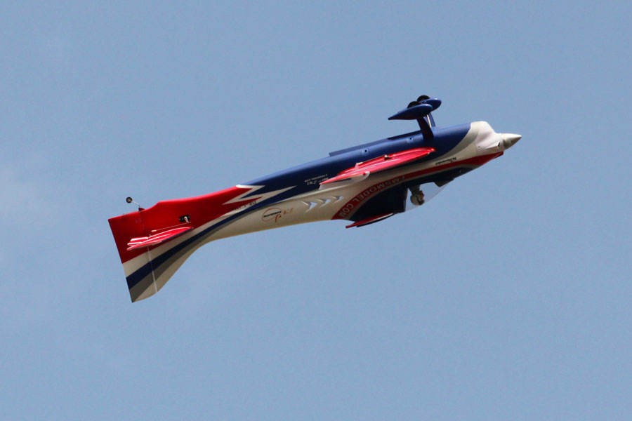 FMS 1400mm F3A Olympus PNP aerobatic RC airplane in blue, white, and red, flying against a blue sky.