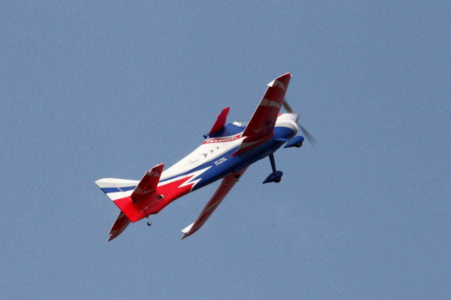 FMS 1400mm F3A Olympus PNP aerobatic RC airplane in red, white, and blue, flying against a blue sky.