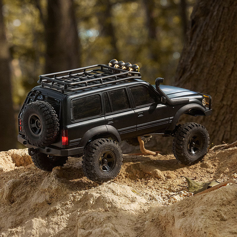 Black FMS 1:18 LC80 Toyota Land Cruiser 80 RTR RC crawler with roof rack and snorkel driving on dirt terrain.