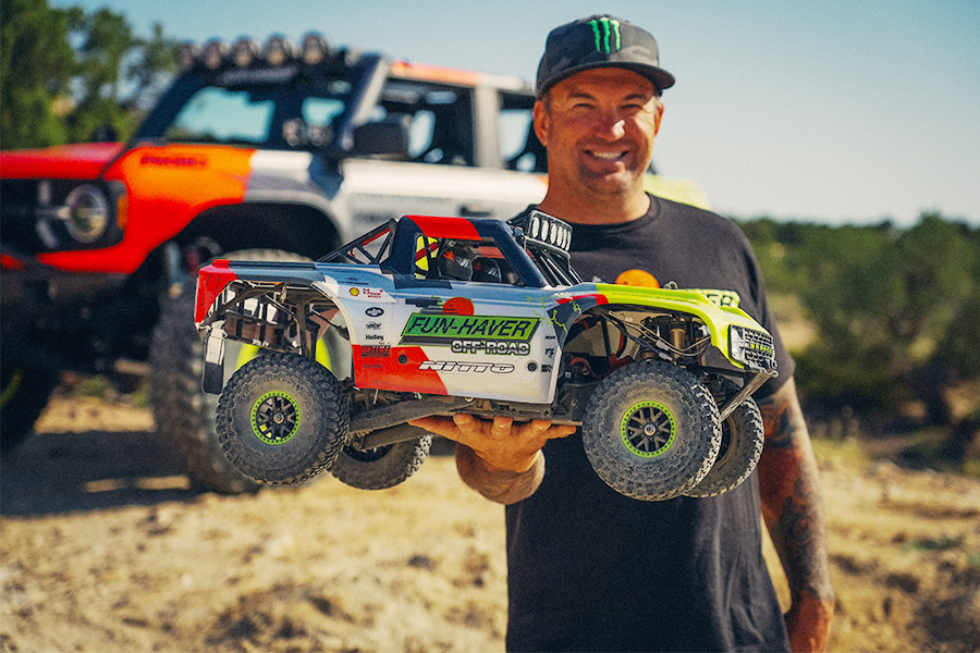 Man holding a Fun-Haver off-road RC trophy truck outdoors with a full-size off-road vehicle in the background