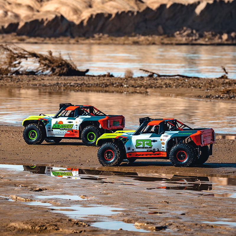 FMS 1:7 Ford Bronco RTR EB Brushless 4WD RS RC trucks parked on a sandy shore with water reflections.