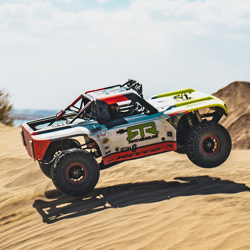 FMS 1:7 Ford Bronco RTR EB Brushless 4WD RS RC truck mid-air jump. White, red, green graphics; "RTR VEHICLE", "NITTO" branding. Off-road.