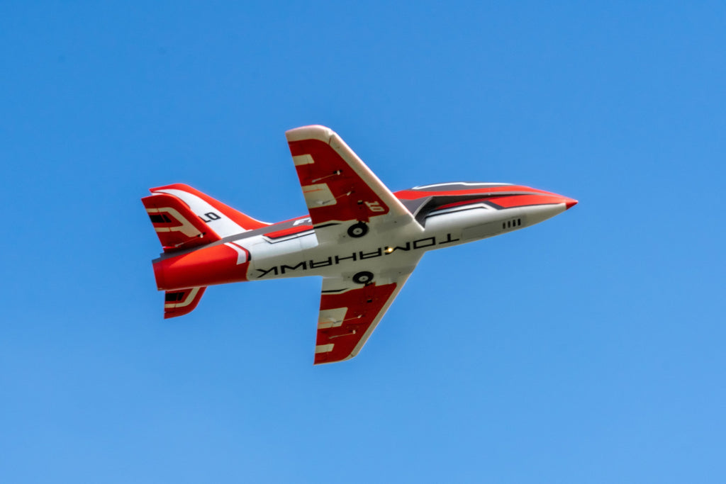 Underside view of the FMS Futura V3 in flight, revealing the "TOMAHAWK" branding and retracted gear positions