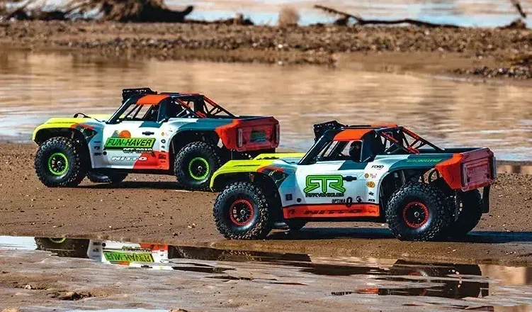 FMS 1:7 Ford Bronco RTR EB Brushless 4WD RS RC trucks parked on a sandy shore with water reflections.