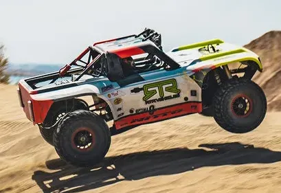 An off-road RC trophy truck with RTR livery jumping over desert sand dunes