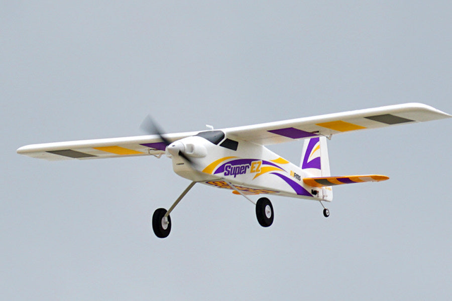 FMS 1220mm Super EZ V4 RC airplane in flight, featuring purple and yellow decals and 'Super EZ' branding.