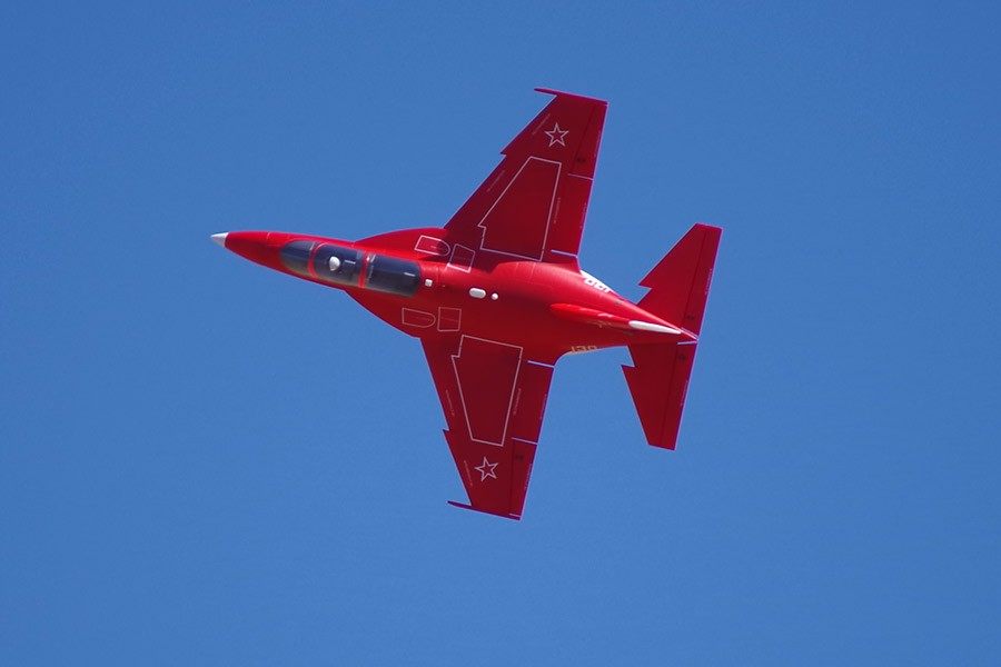 Red FMS 70mm Yak-130 V2 EDF jet in flight against a clear blue sky, showcasing its detailed scale features.