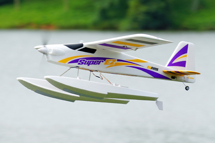 FMS 1220mm Super EZ V4 RC plane with floats flying over water. White with purple/yellow graphics.