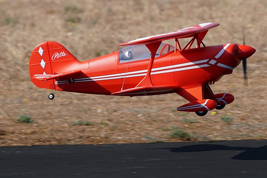 Red FMS 1400mm Pitts V2 biplane model aircraft flying with white stripe details.