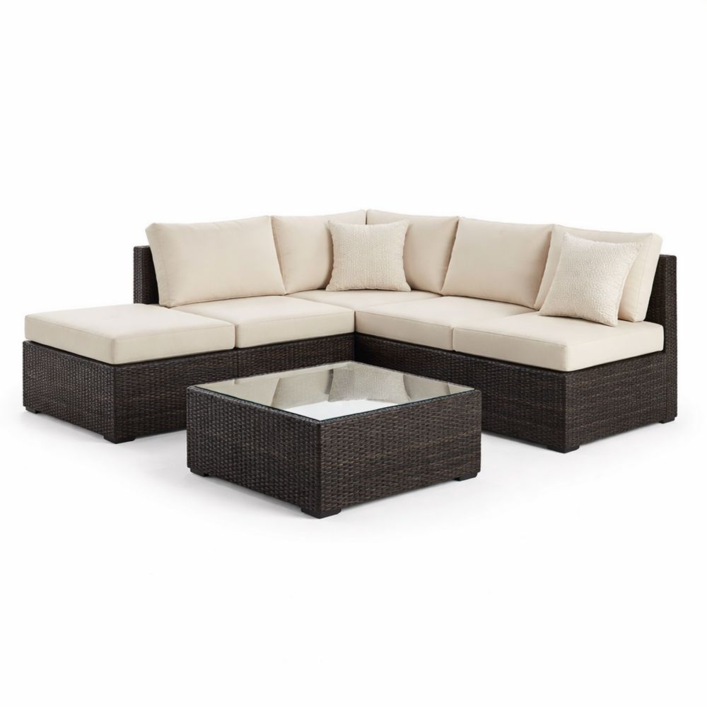 Canapé d'angle en résine tressée avec coussins beiges et table basse en verre