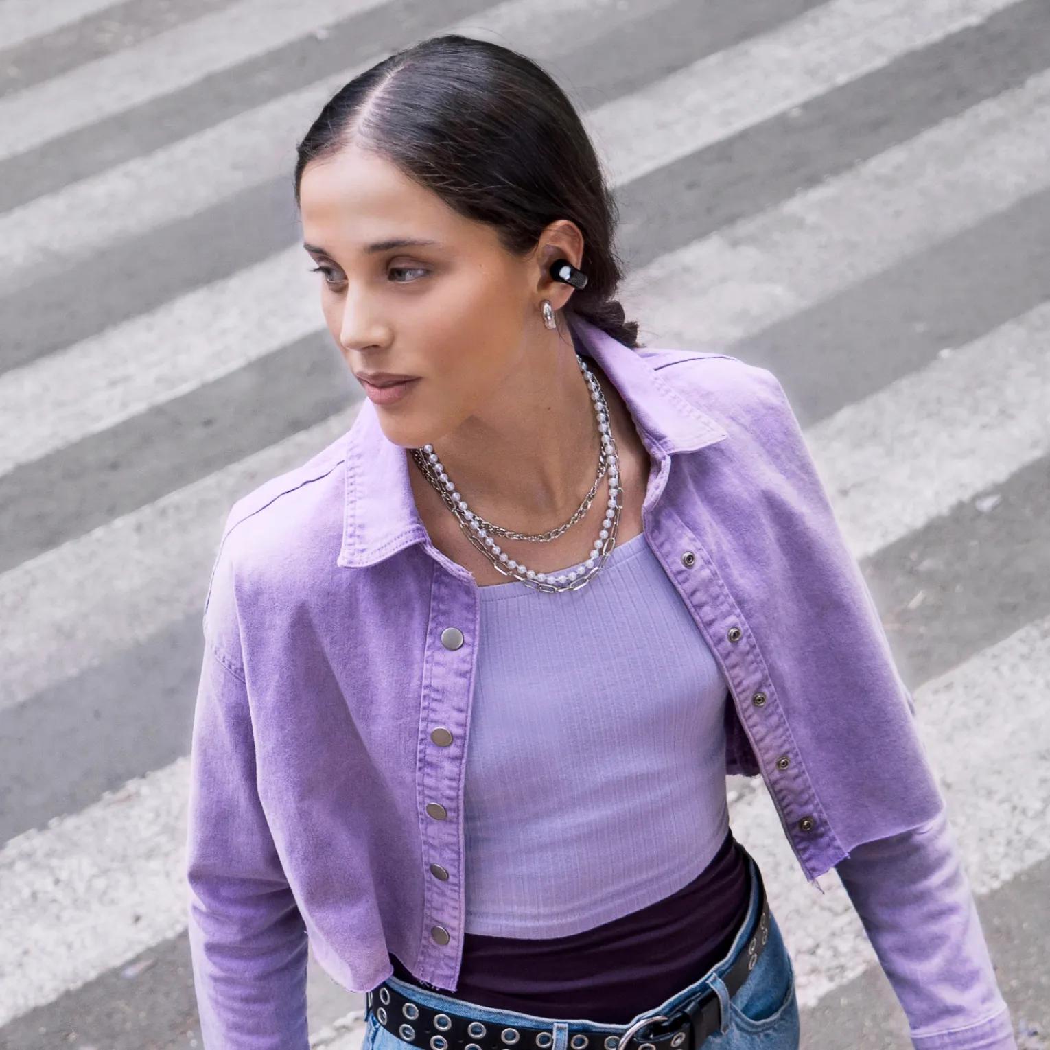 Woman wearing Bose Ultra Open Earbuds crossing the street outside.