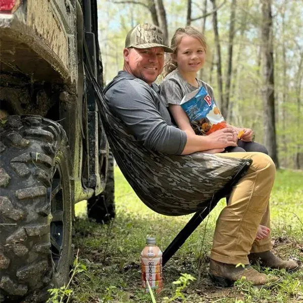 Adult and child seated beside a vehicle in a woodland setting