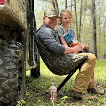 Adult and child seated beside a vehicle in a woodland setting