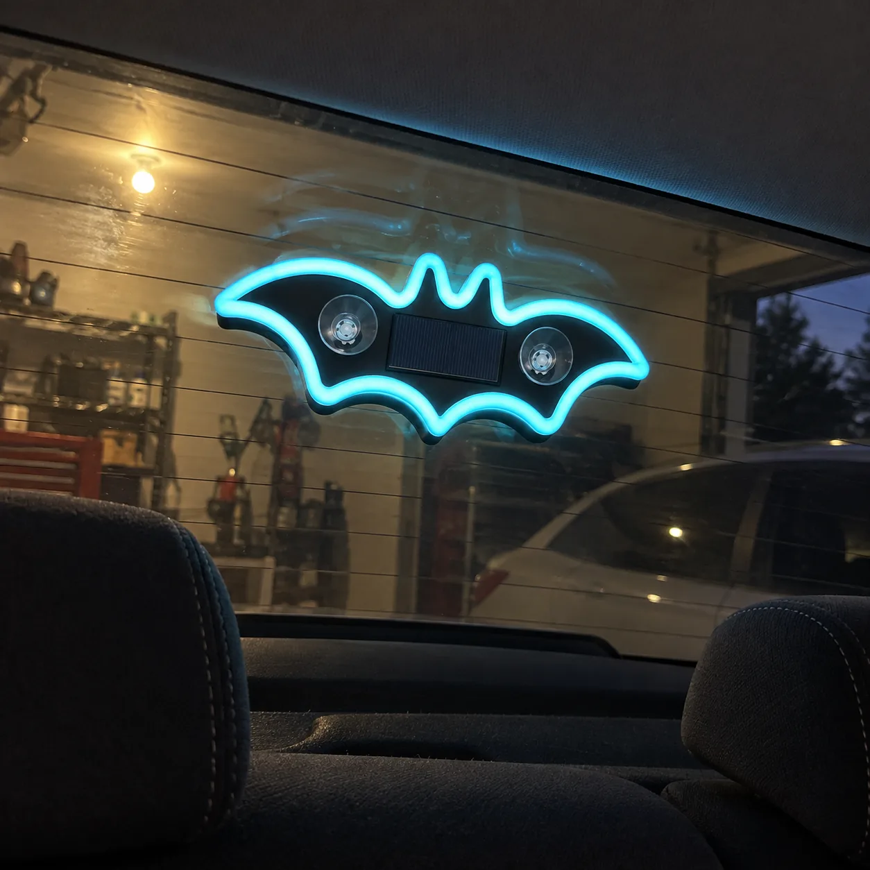 Cyan bat light on a car rear window near a garage