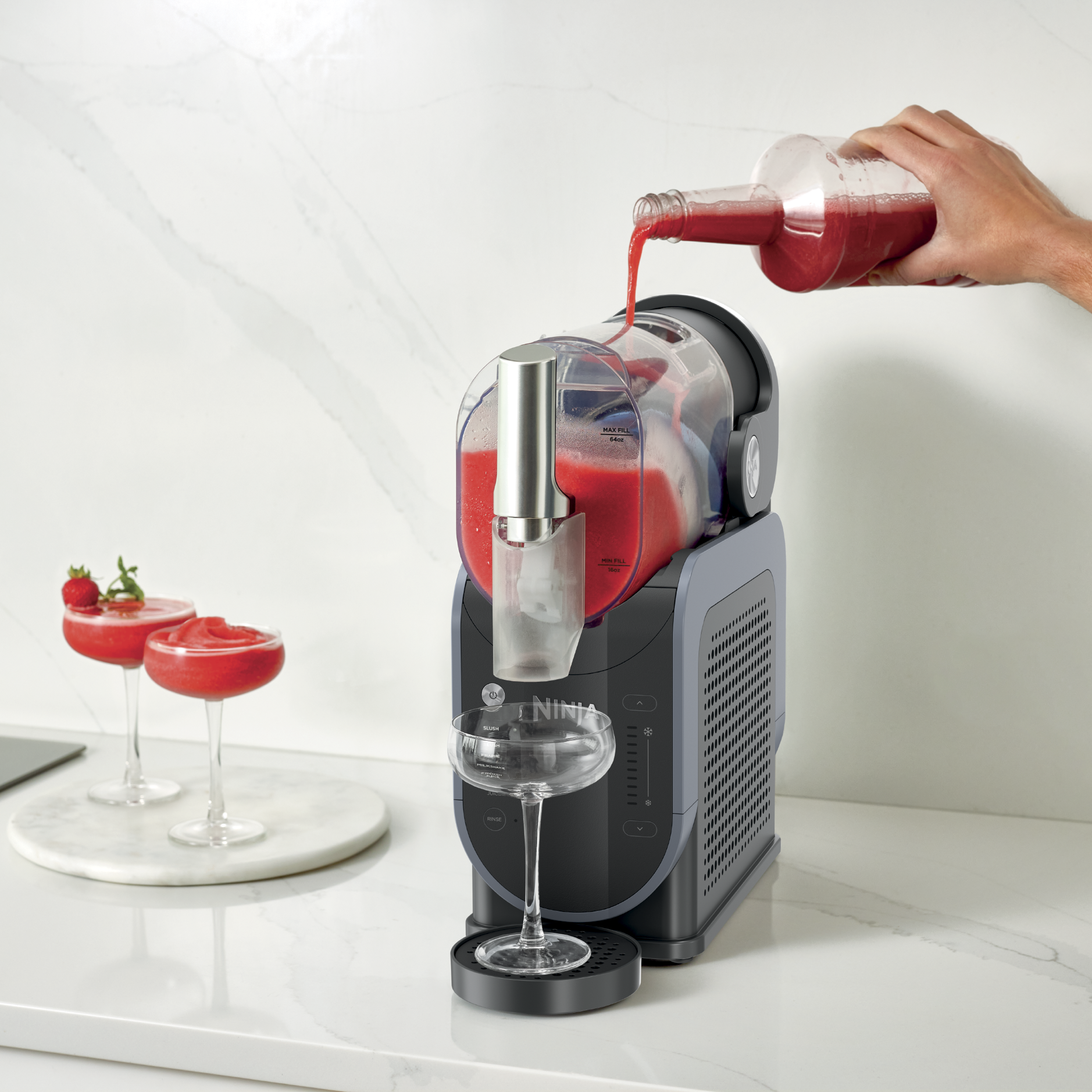 Personne versant du jus dans la machine à slush, avec deux verres de slush sur le côté gauche.