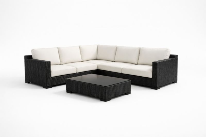 Divano angolare in rattan nero con cuscini bianchi e tavolino in vetro