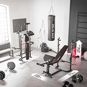 Home gym setup with weight bench, squat rack, punching bag, dumbbells, and various exercise equipment in a white-walled room.