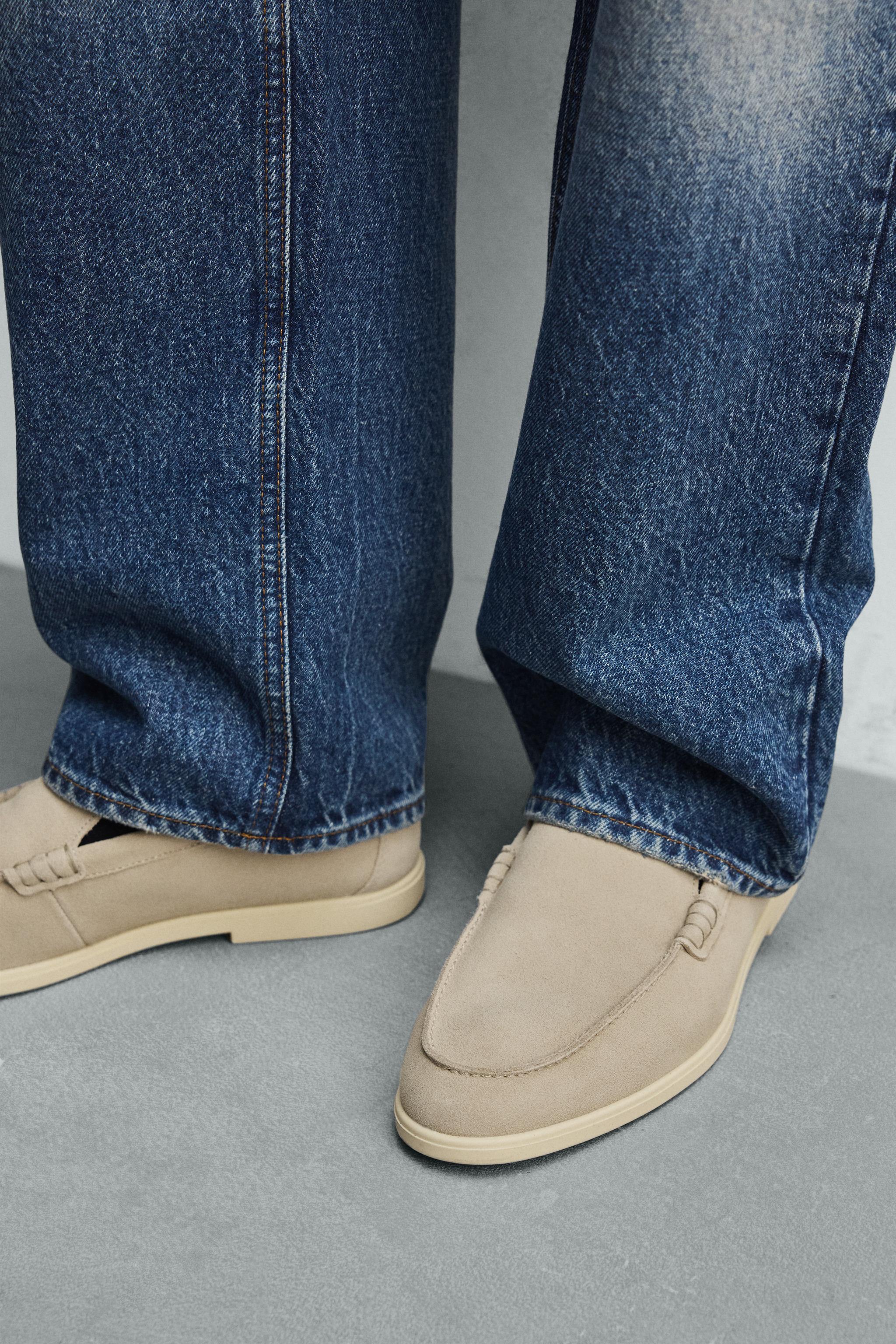 Mid-shot of loafers with a penny strap and contrasting sole, paired with blue jeans.