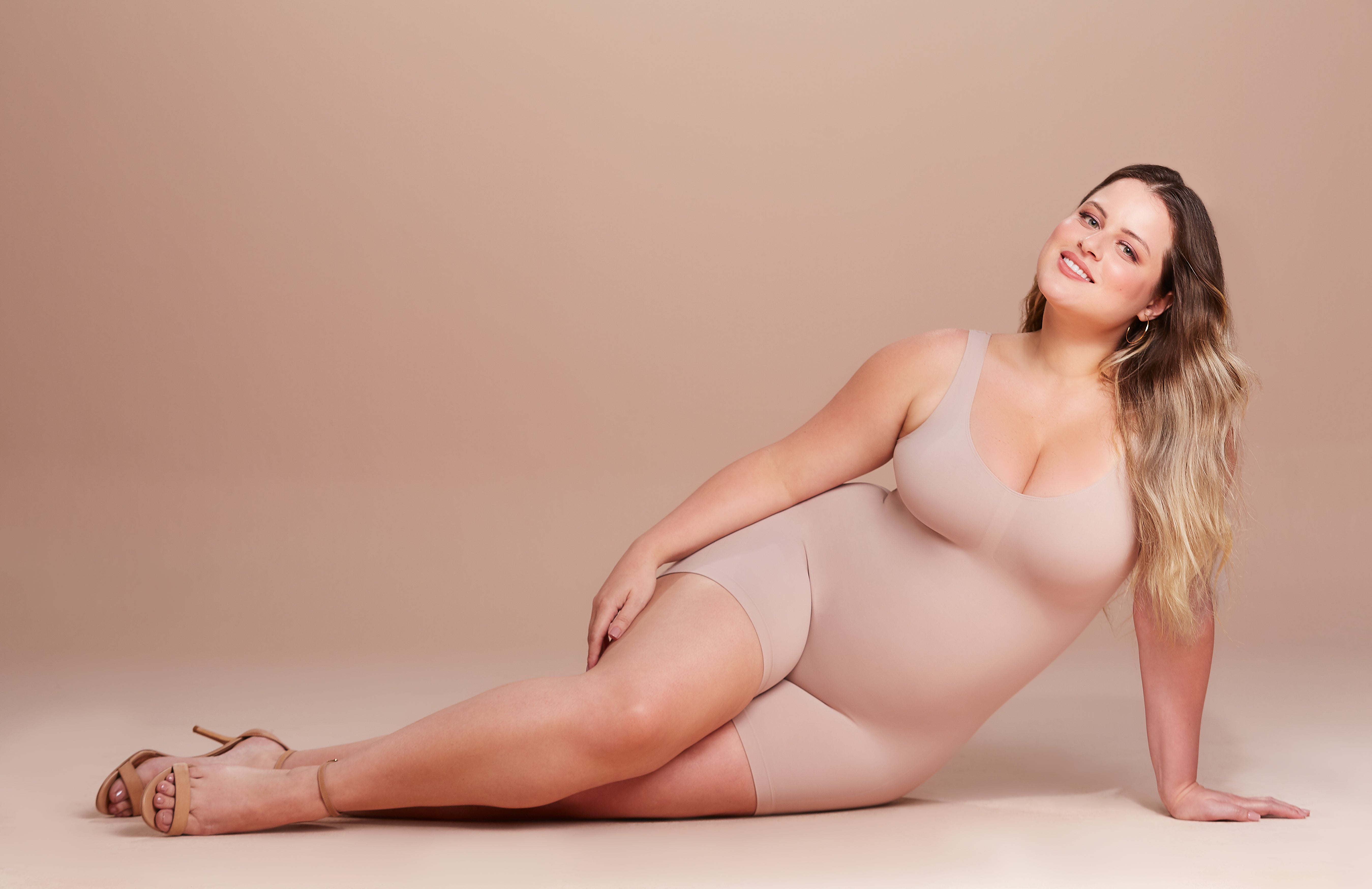Model sitting and wearing Emana Body bodysuit in base color