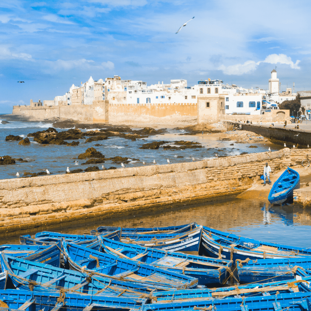 Morocco eSIM – Blue fishing boats moored at Essaouira harbour with historic white medina walls along the Atlantic coast, travel eSIM for Morocco
