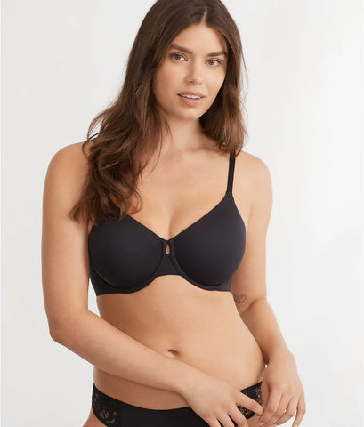 A woman poses in a black bra, showcasing a simple and elegant design. She has long, wavy hair and a neutral expression.