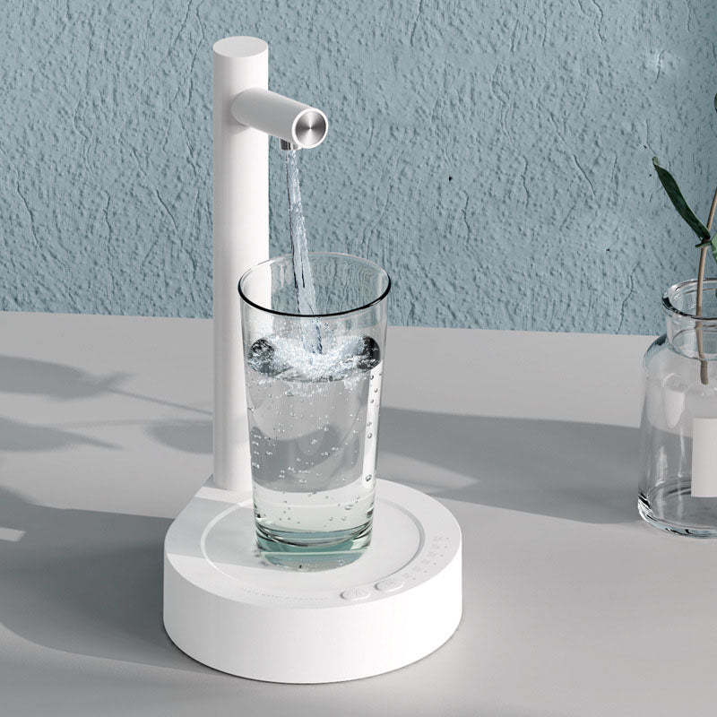 White manual water pump filling a glass with water on a light gray surface.