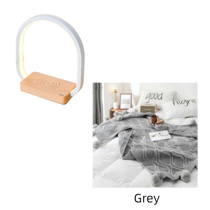 Table lamp with wooden base on a white background, next to a bedroom scene with a blanket and pillows.
