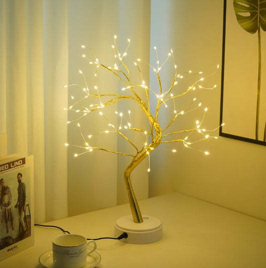 Decorative LED tree on a table with a cup and saucer in a softly lit room.