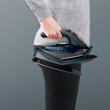 Person carrying the cordless steam iron with its base, showing easy portability and compact storage design.