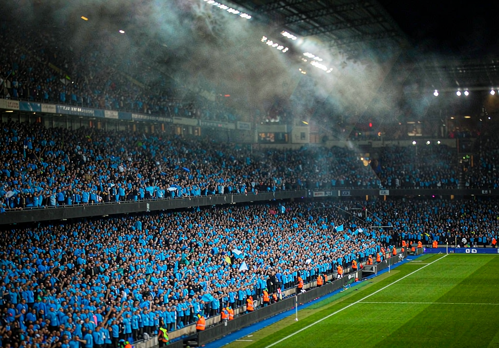 Manchester City fans at Etihad Stadium with sky blue flags