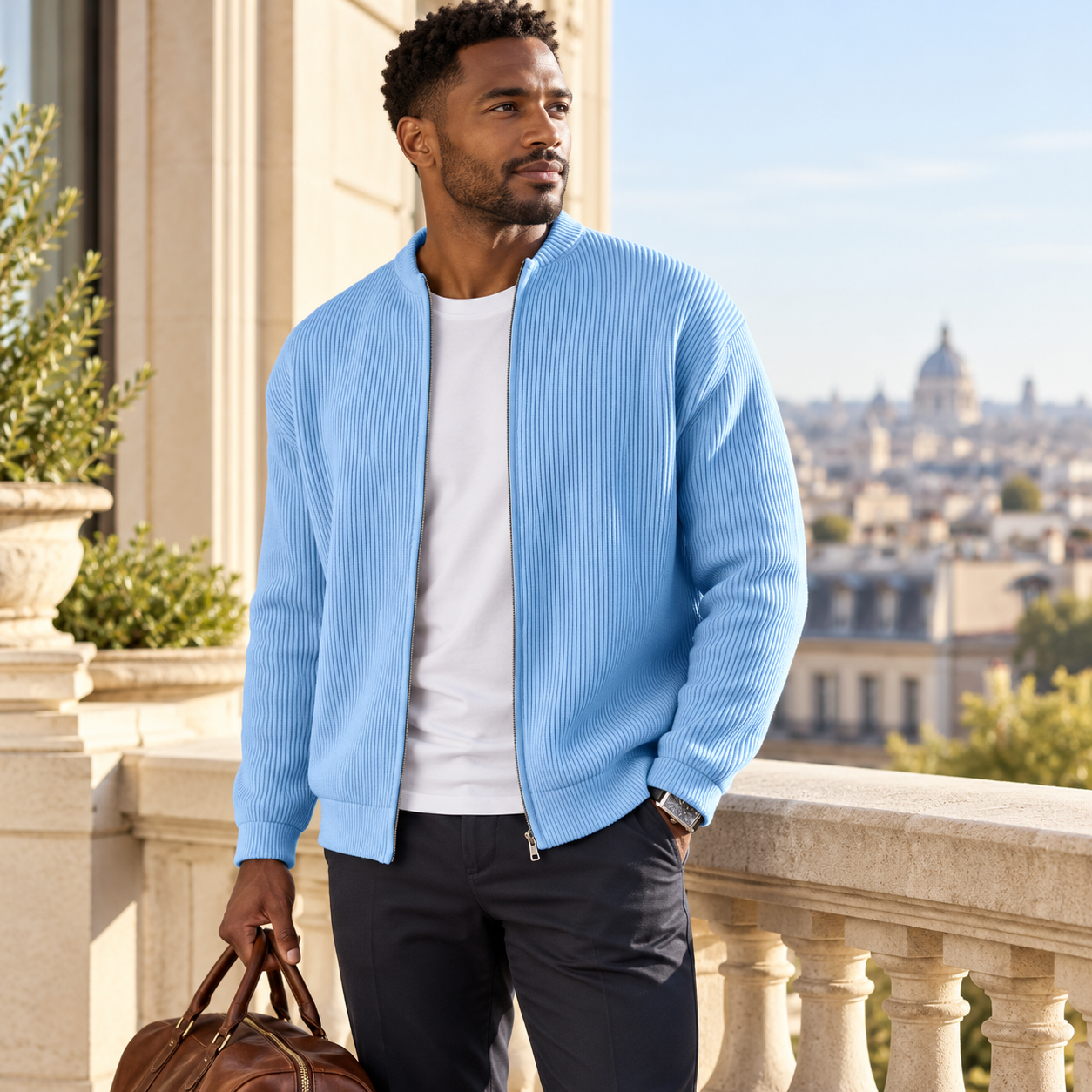 Man by a hotel balcony holding a brown weekend bag in the blue ribbed jacket