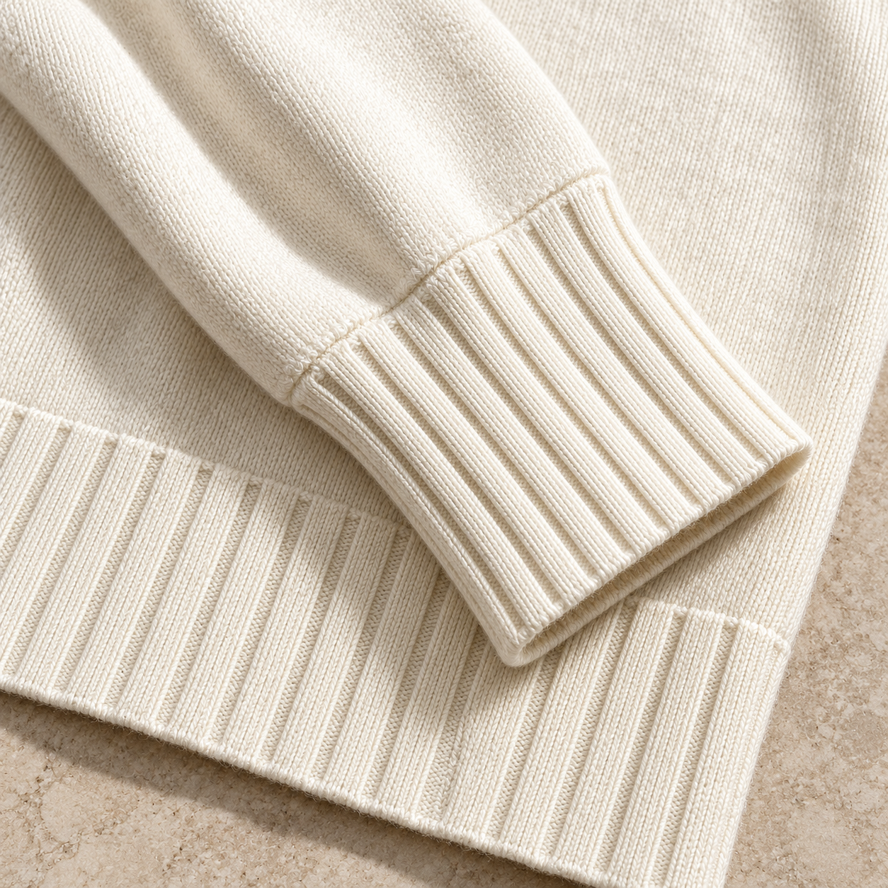 Close-up of ivory smooth knit fabric and broad ribbed sleeve cuff