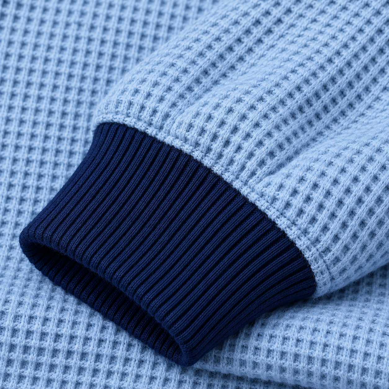 Macro of light blue waffle-knit fabric next to the navy ribbed cuff