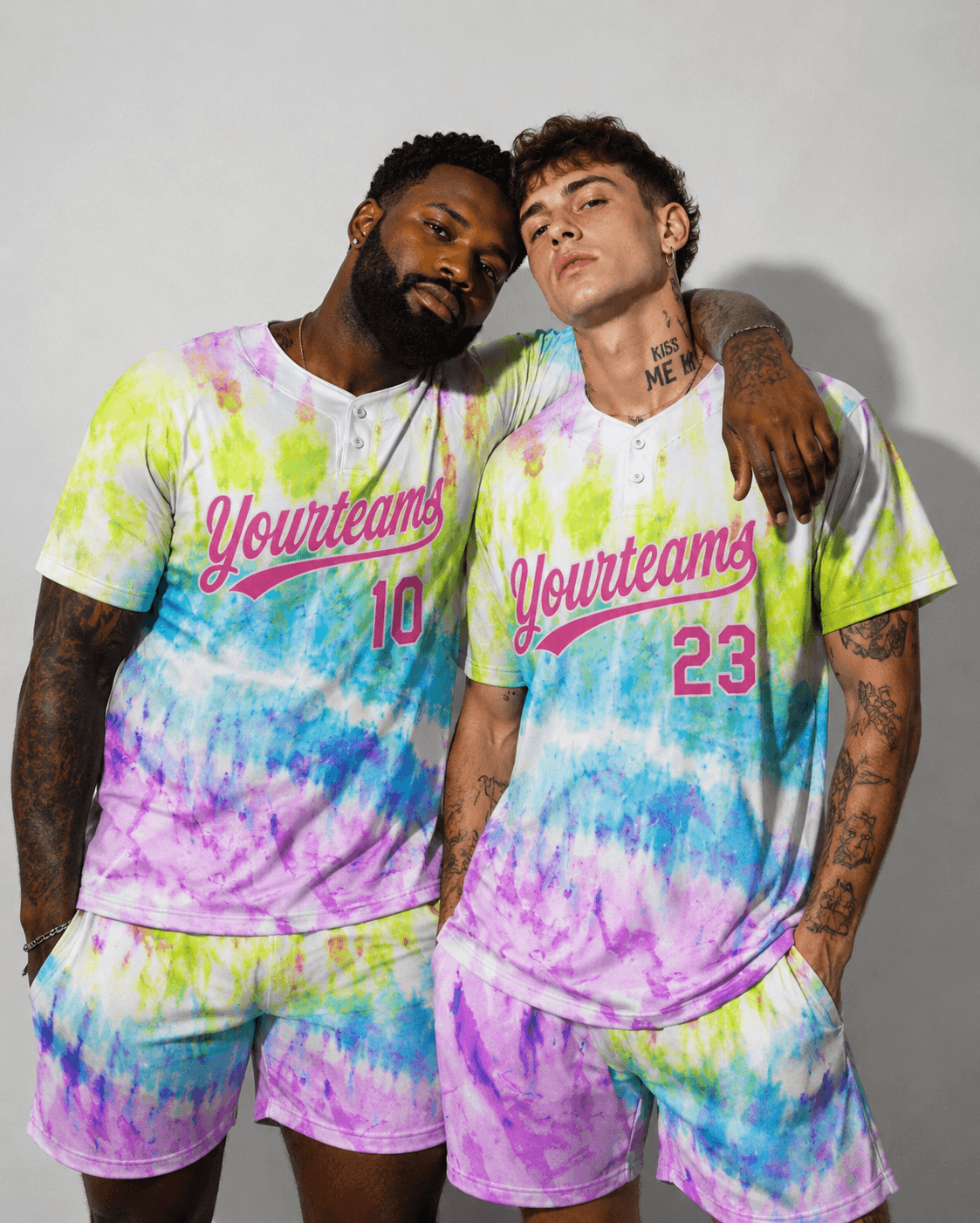 Two male models posing in a studio, wearing matching pastel tie-dye pride jerseys and shorts sets.